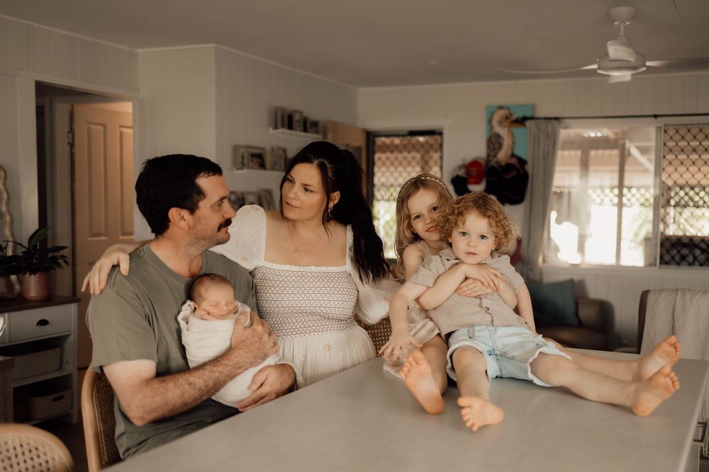 Happy family of five with newborn baby gathered around kitchen counter in bright home interior.