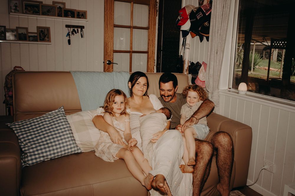 Family of four relaxing together on couch in cozy living room, parents with two young children.