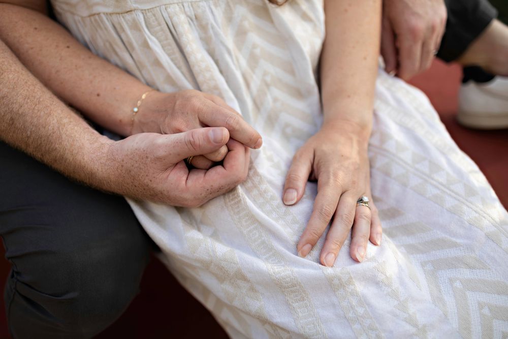 Close-up of couple holding hands, woman wearing diamond ring in white patterned dress.
