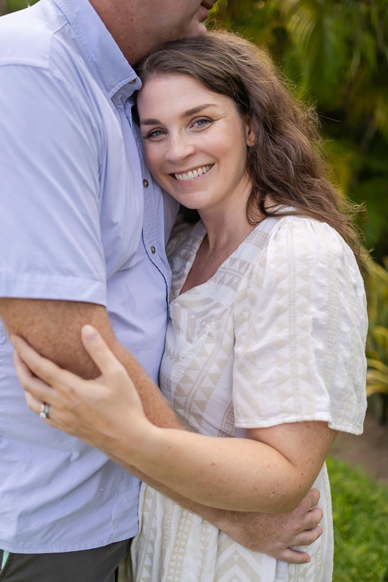 Smiling woman in white dress embraces man outdoors near tropical greenery.
