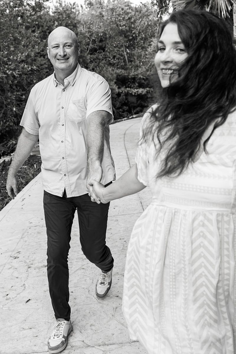 Black and white photo of bald man holding hands with woman on outdoor path.