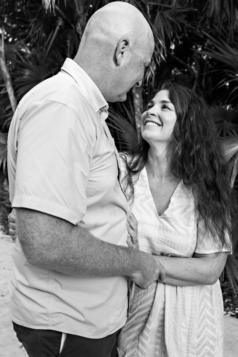 Couple embracing and smiling at each other in black and white photo with tropical palm trees in background.