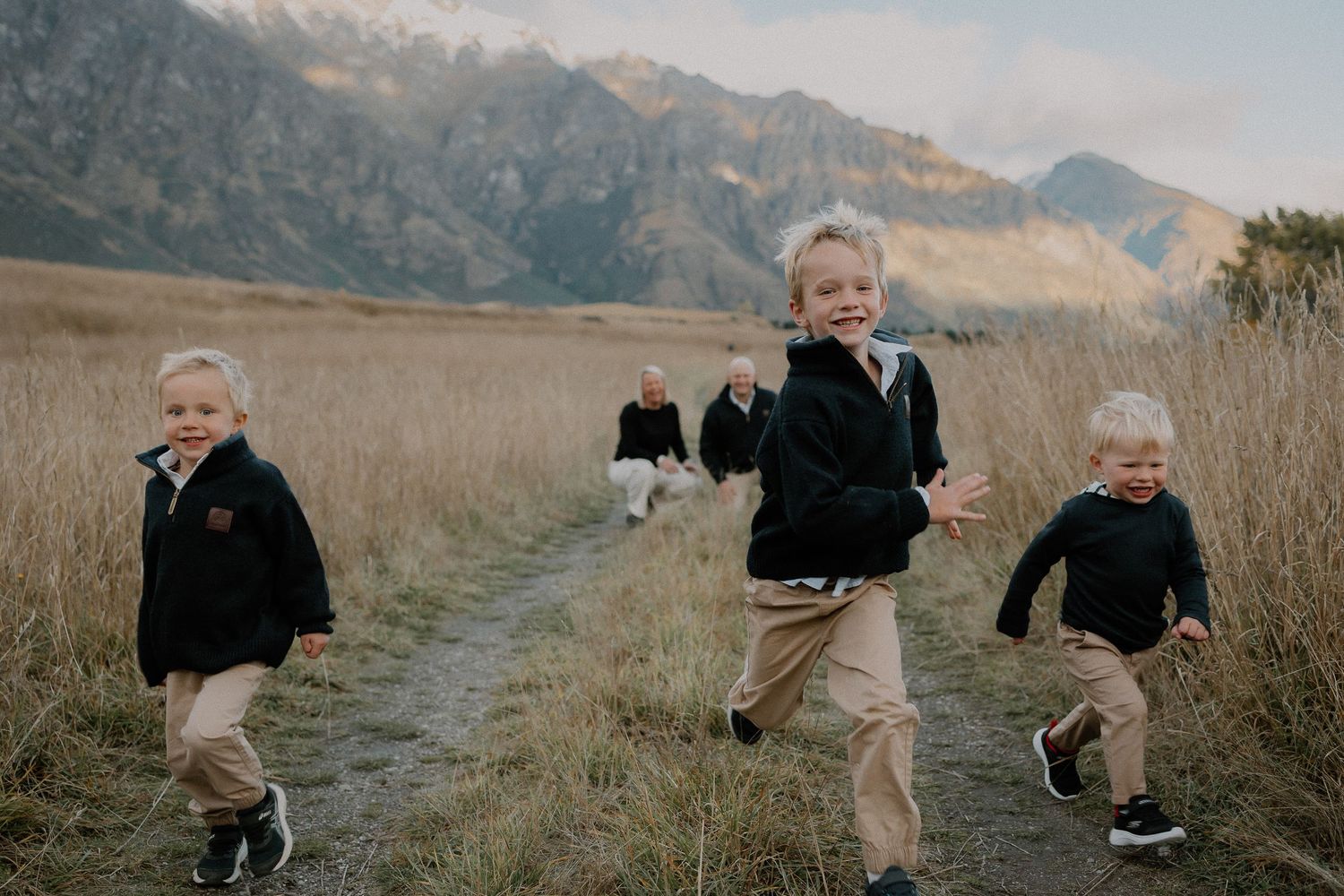 Black and white photo of children running joyfully on a mountain trail through tall grass.