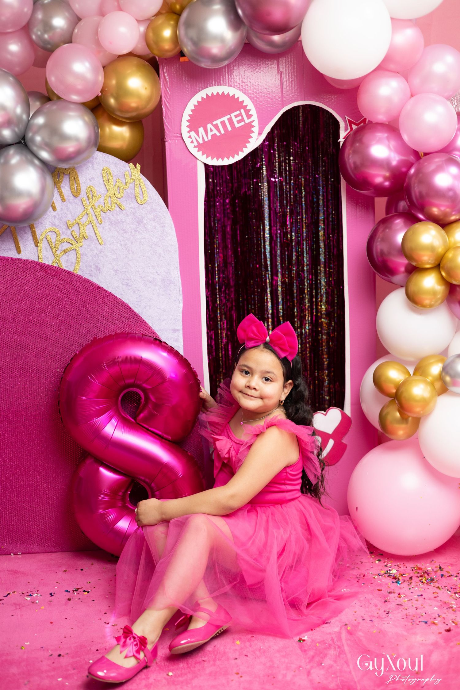 Girl in pink dress poses with number 8 balloon at Mattel-themed birthday party with pink and gold balloon decorations.