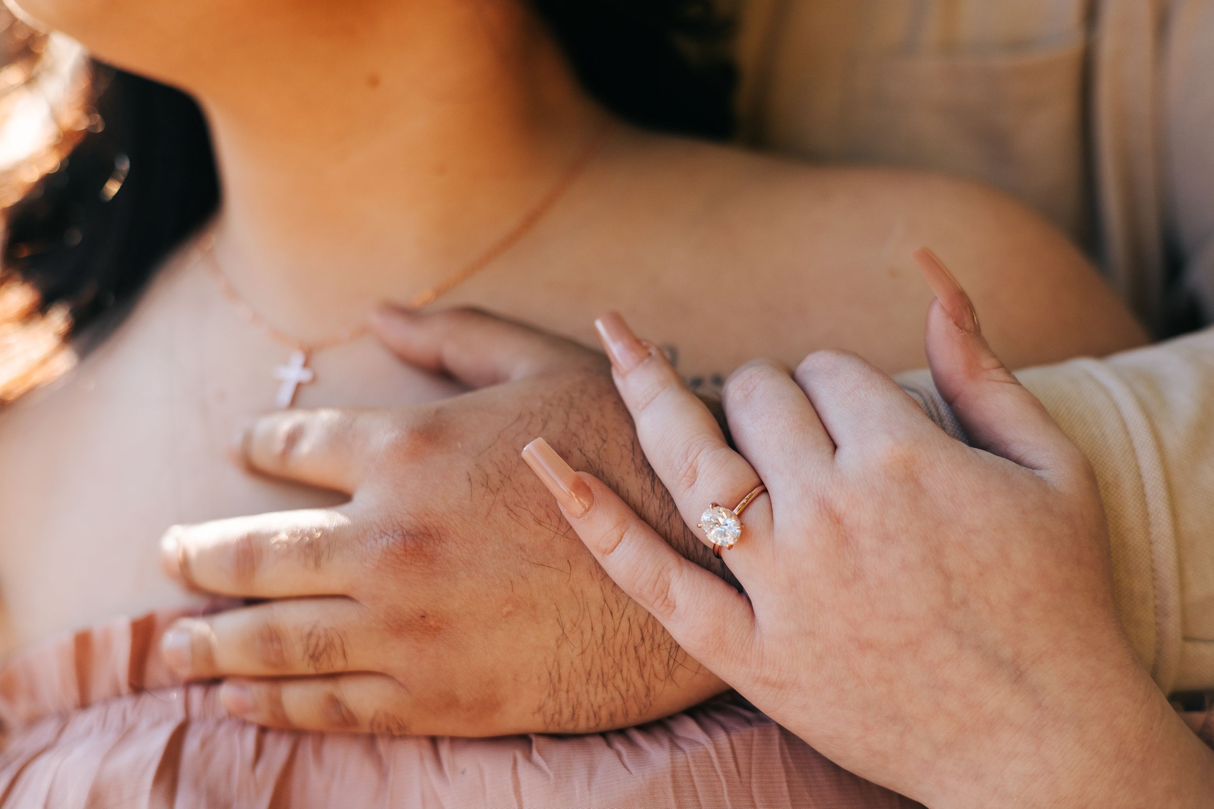 Close-up of a couple embracing, showcasing a stunning oval diamond engagement ring on the woman's finger.
