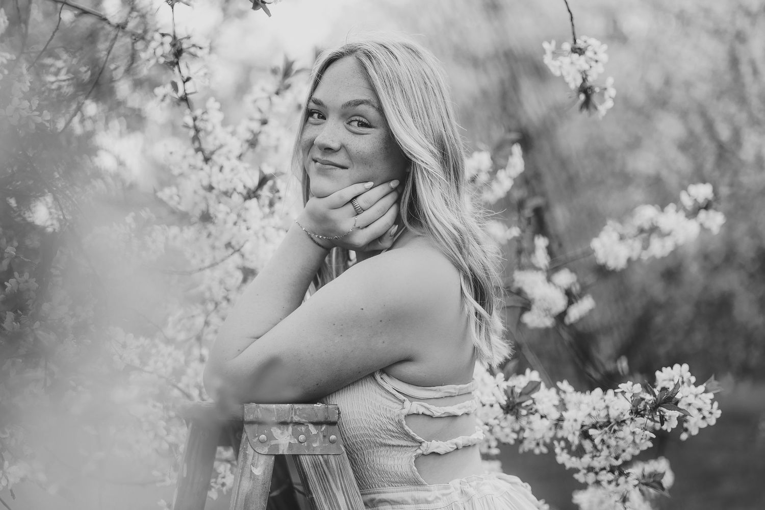 Black and white portrait of a smiling blonde high school senior posing among blooming cherry blossom branches in spring.
