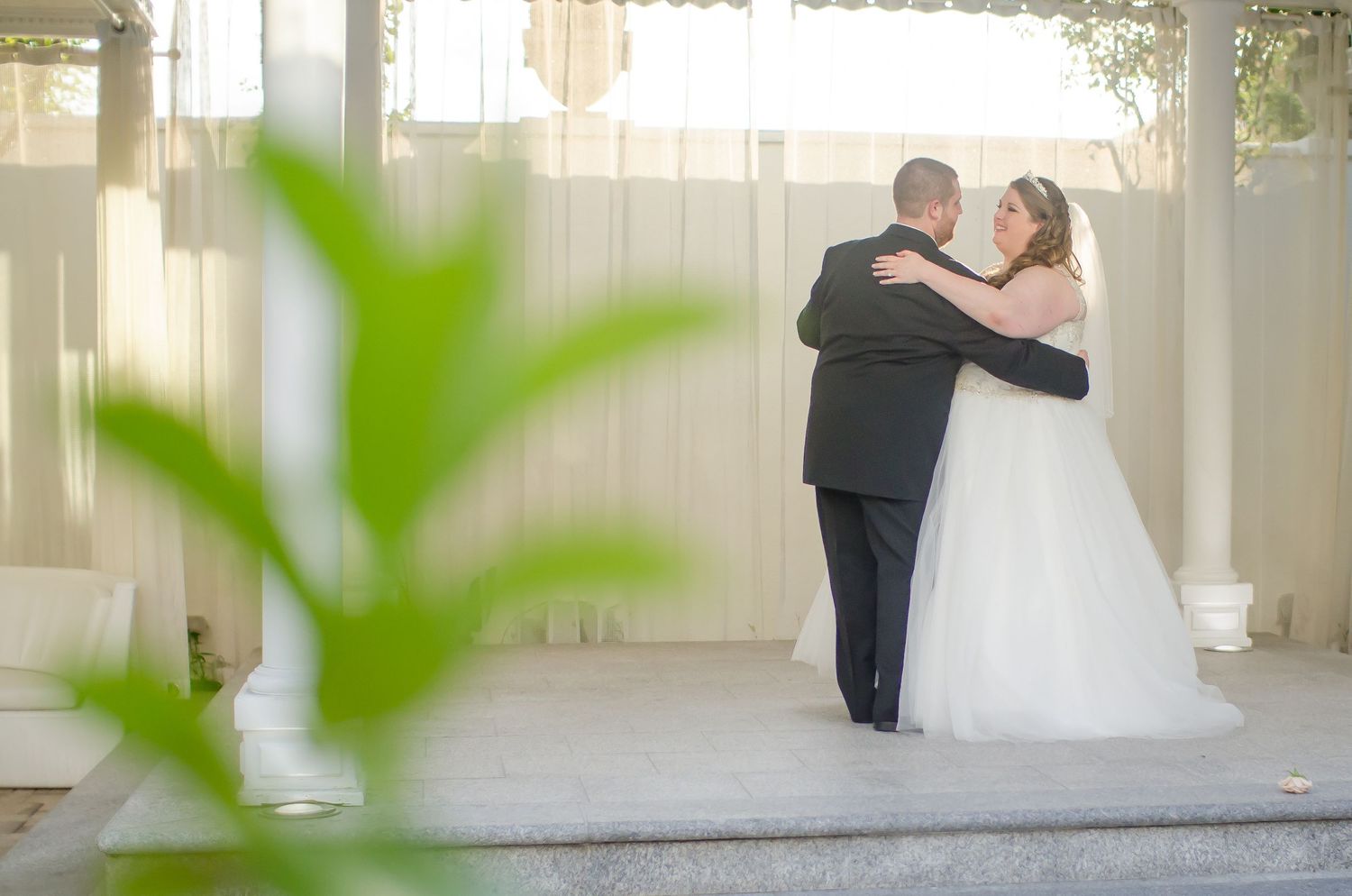 A bride and groom share their first dance outdoors near a white gazebo on their wedding day.
