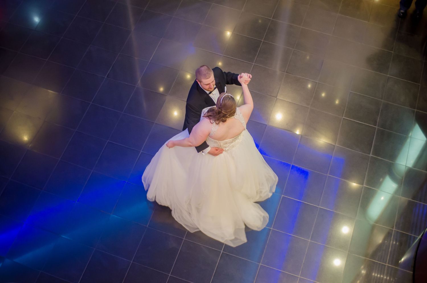 Bride and groom share romantic first dance aerial view on illuminated dance floor with blue lighting.