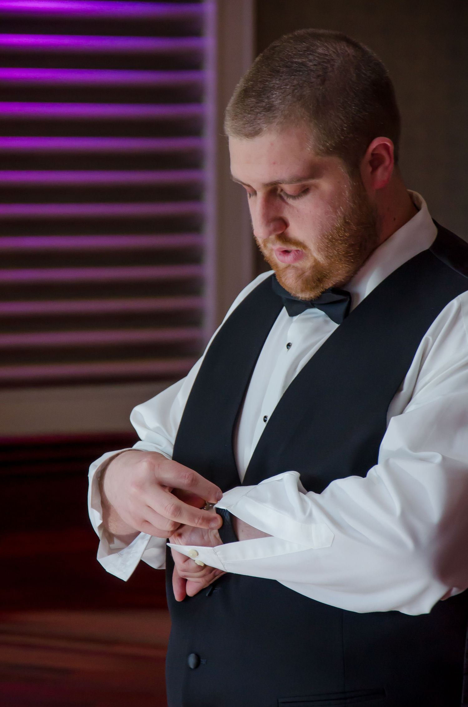 Groom in black vest and bow tie adjusting his cufflinks while getting ready for his wedding ceremony.