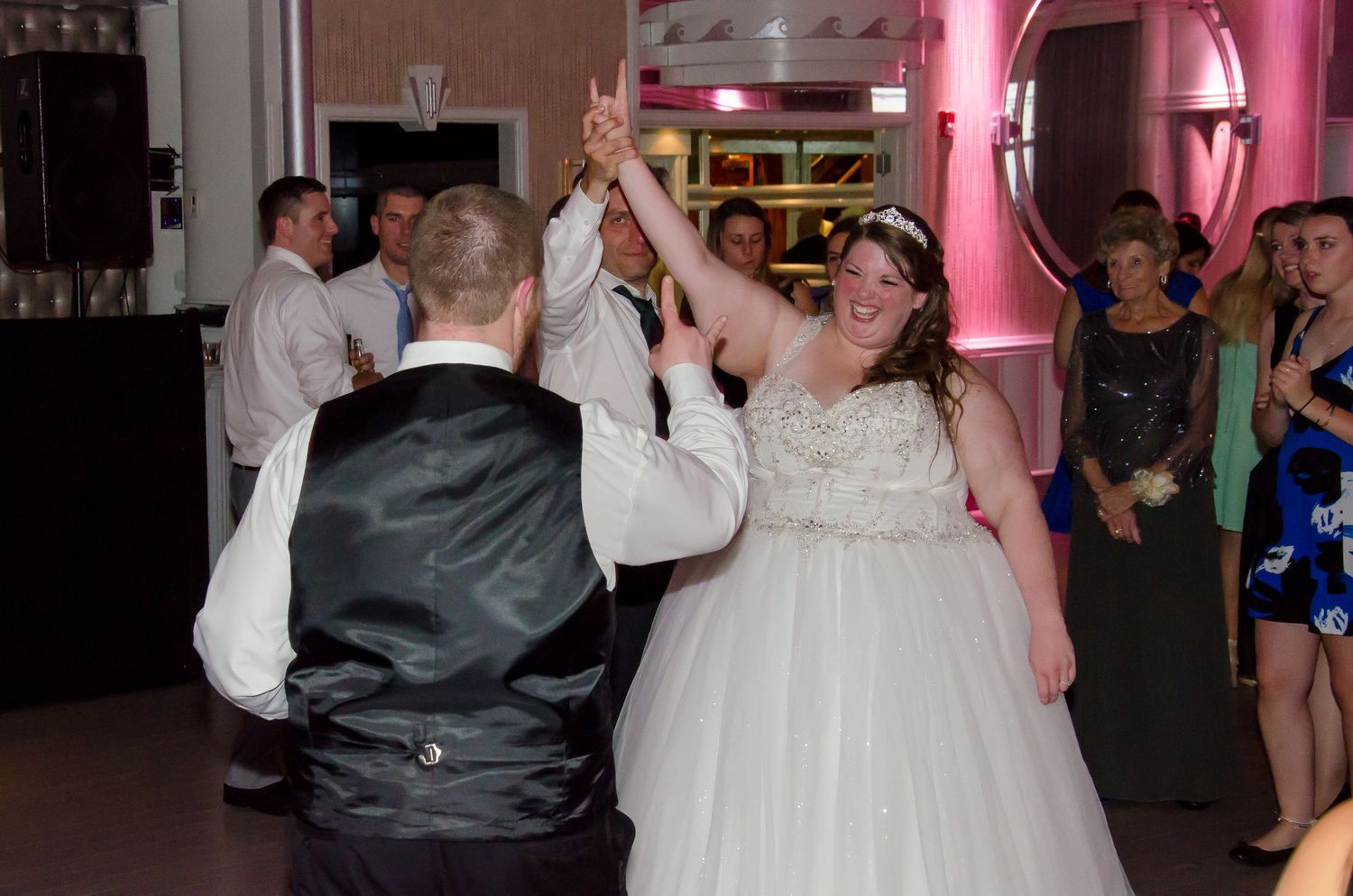 Bride and groom share their first dance at a wedding reception, surrounded by guests in an elegantly lit ballroom.
