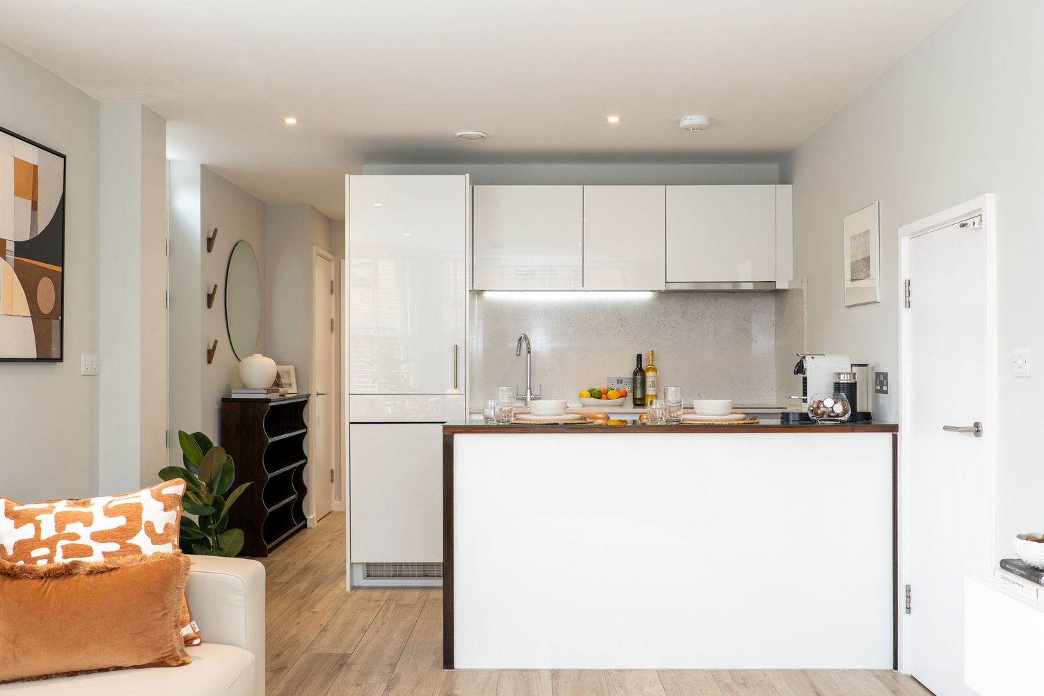Modern open-plan kitchen with white gloss cabinets, wooden countertop island, and light wood flooring in a compact apartment.