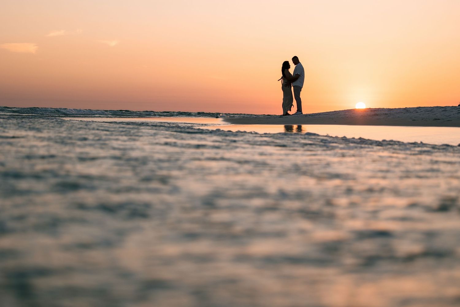 couple being photographed hugging during sunset at the water and beach line