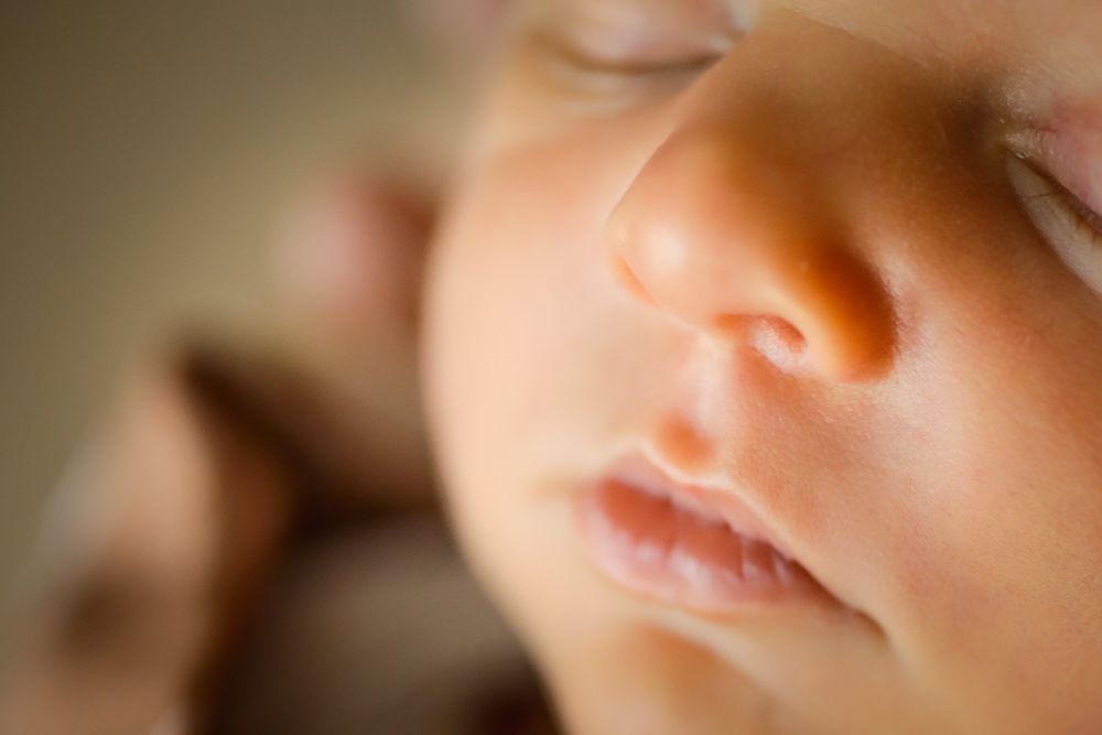 Close-up macro photo of a sleeping newborn baby's face with soft skin and delicate features.