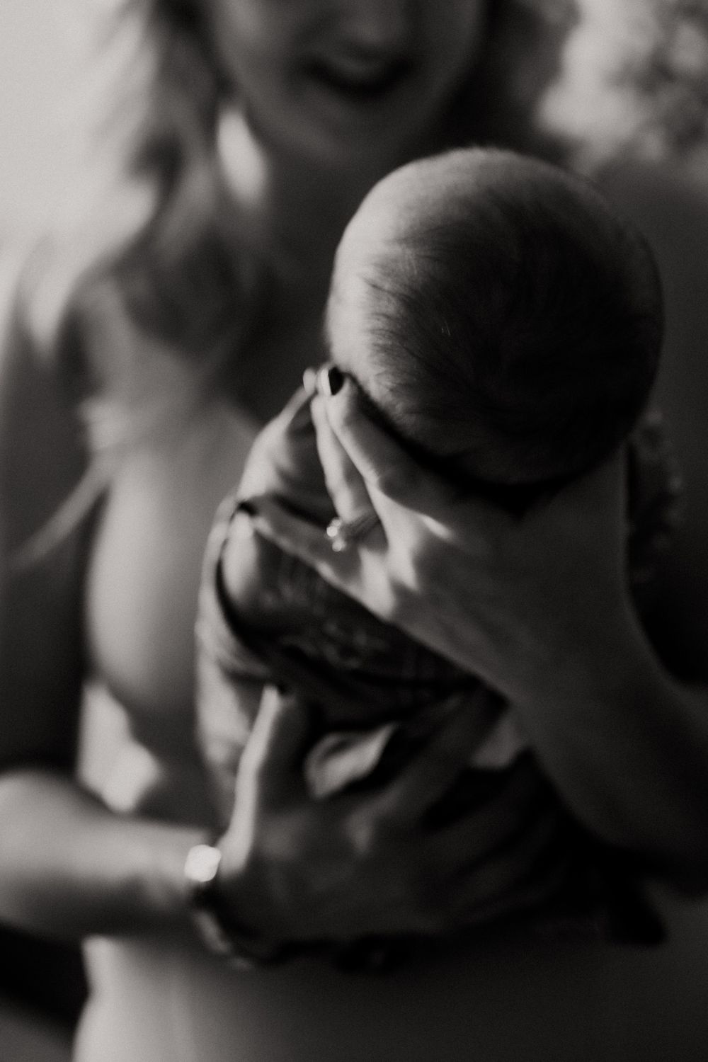 Black and white photo of a smiling mother tenderly cradling her newborn baby, wearing a diamond ring.