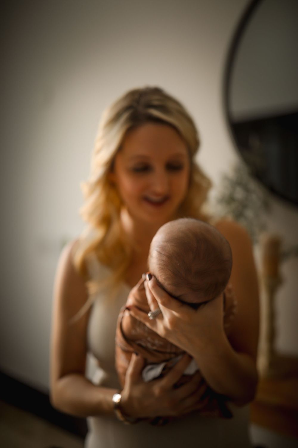 Soft focus image of blonde mother gazing lovingly at swaddled newborn baby she holds up.