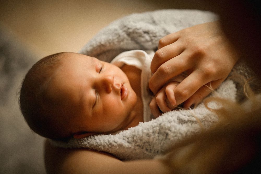 Newborn baby sleeping peacefully in a soft blanket while being cradled in a parent's arms.