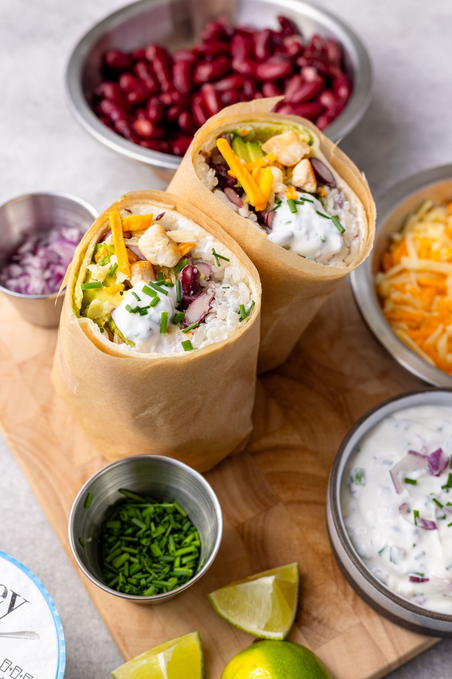 Fresh Mexican wraps served with colorful toppings including shredded cheese, red onions, and lime wedges on a wooden board.