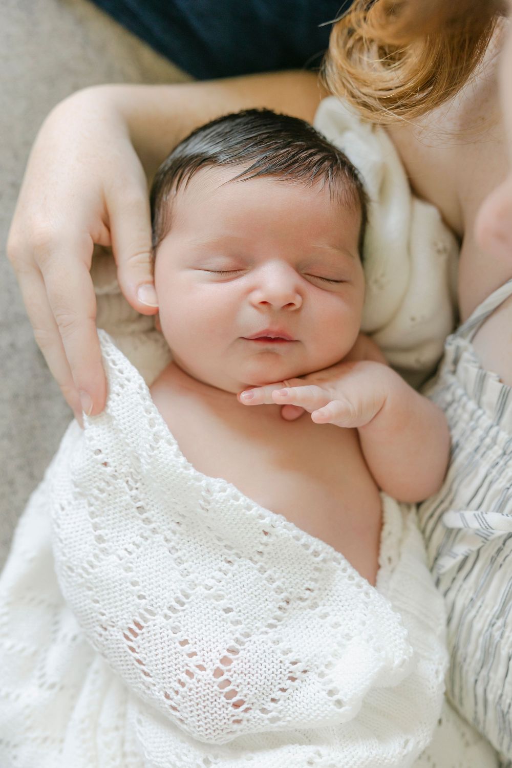 Peaceful newborn baby sleeping wrapped in white knit blanket, cradled gently in mother's arms.