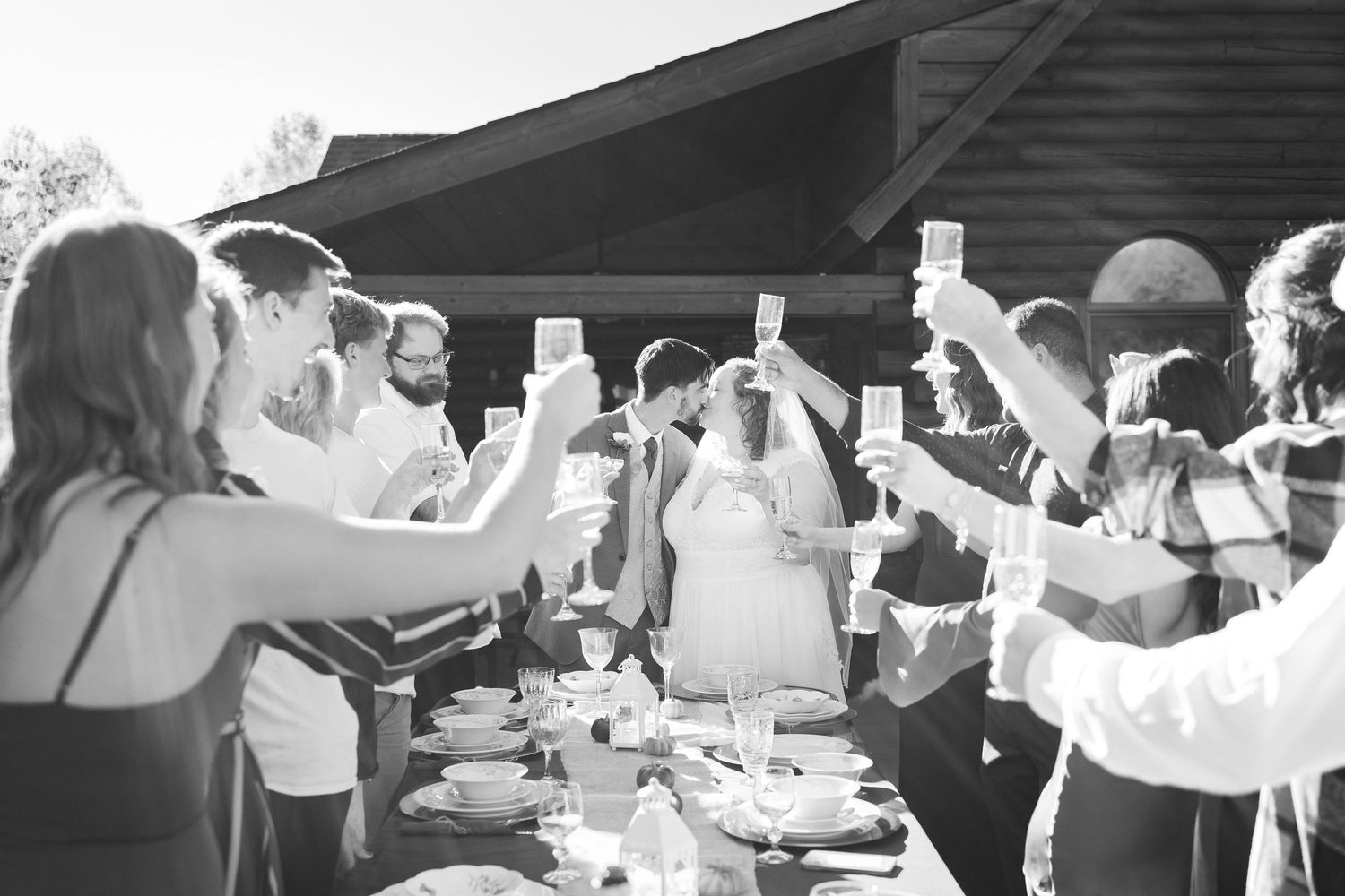 Wedding guests raising glasses in a toast at an outdoor reception dinner table on a sunny day. Hocking Hills wedding airbnb Elopement
