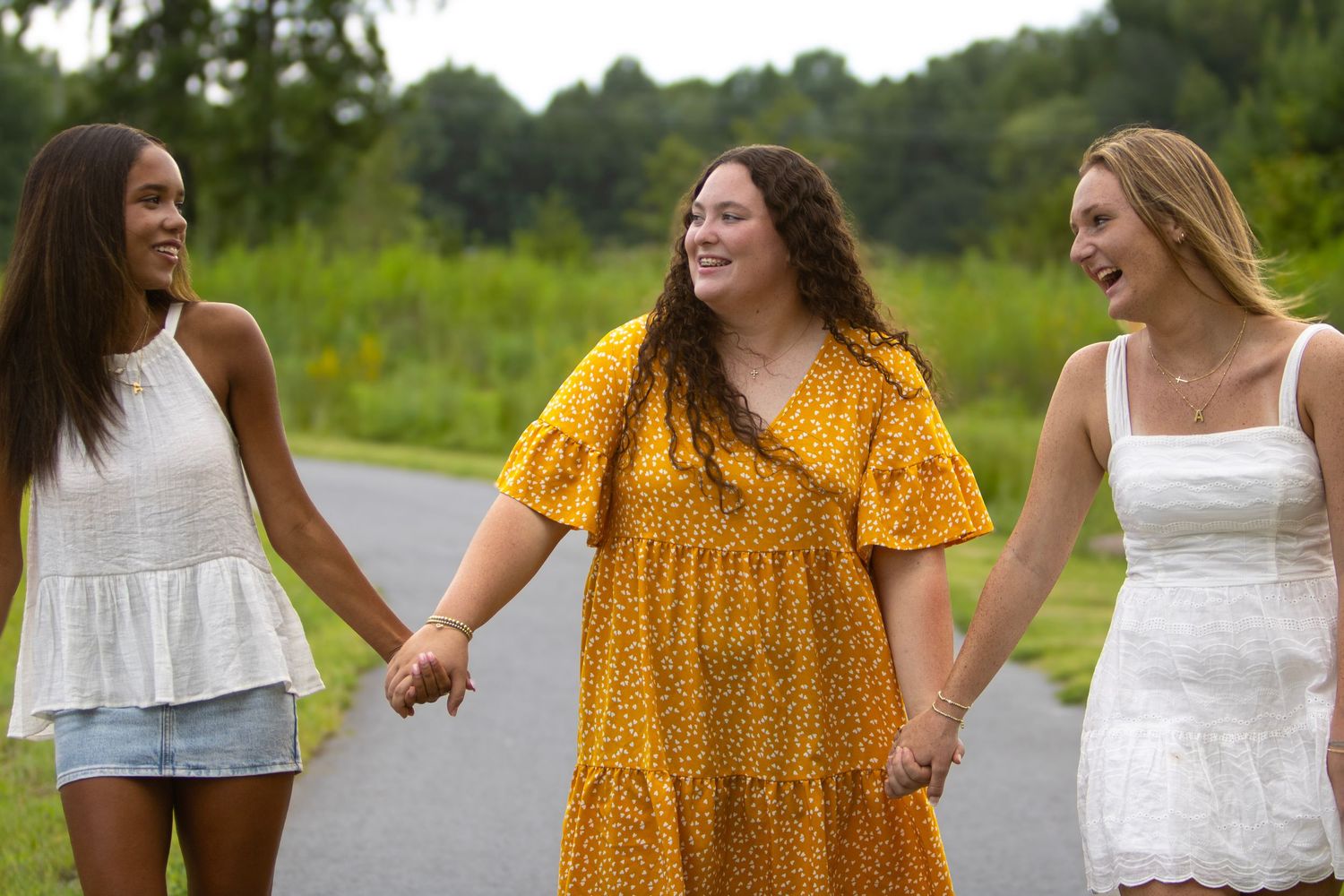 Three young women in white dresses smile together in a flower field in this black and white portrait photo.