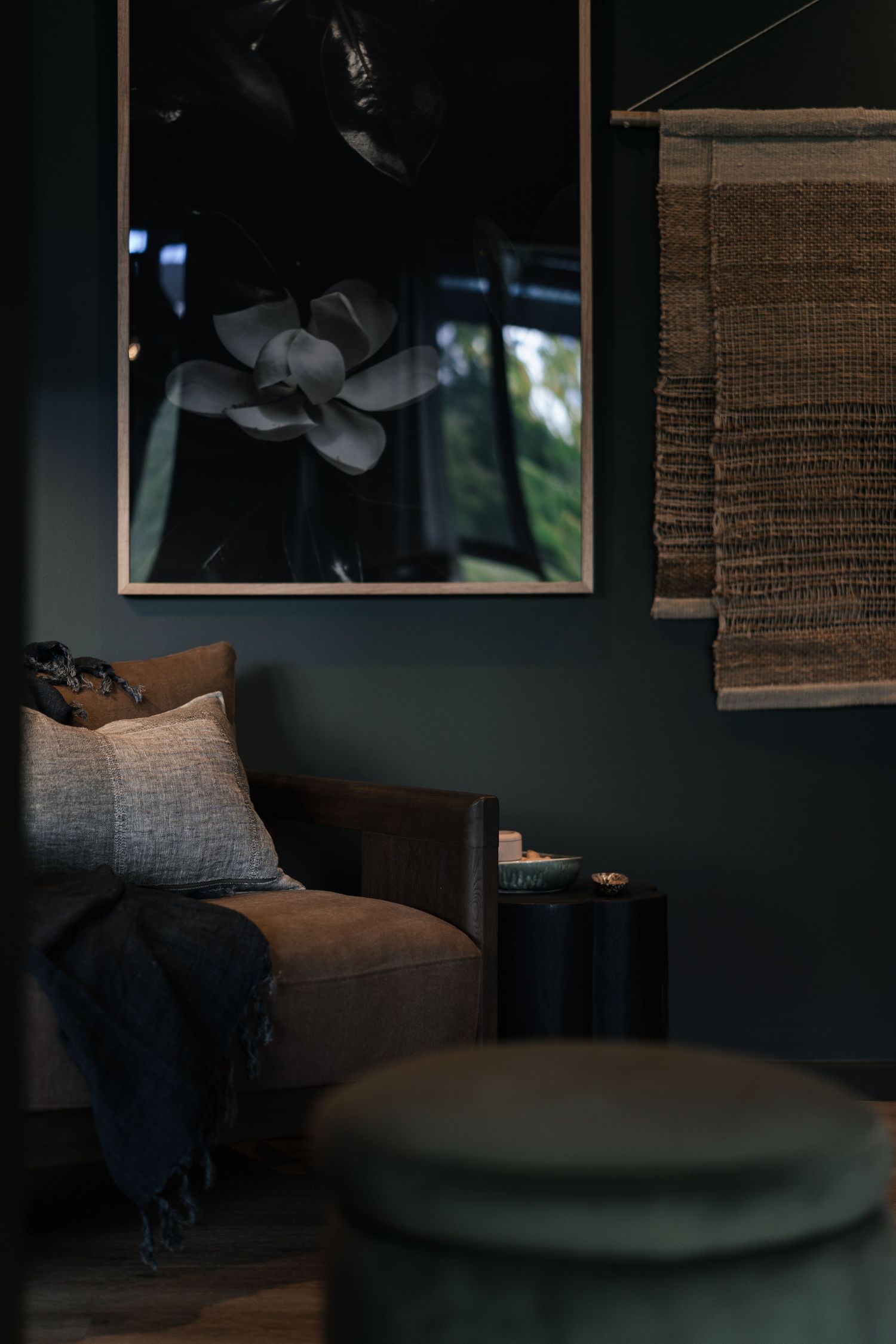 Dark moody living room with forest green walls, botanical artwork, woven wall hanging, and velvet ottoman.

The Empress
