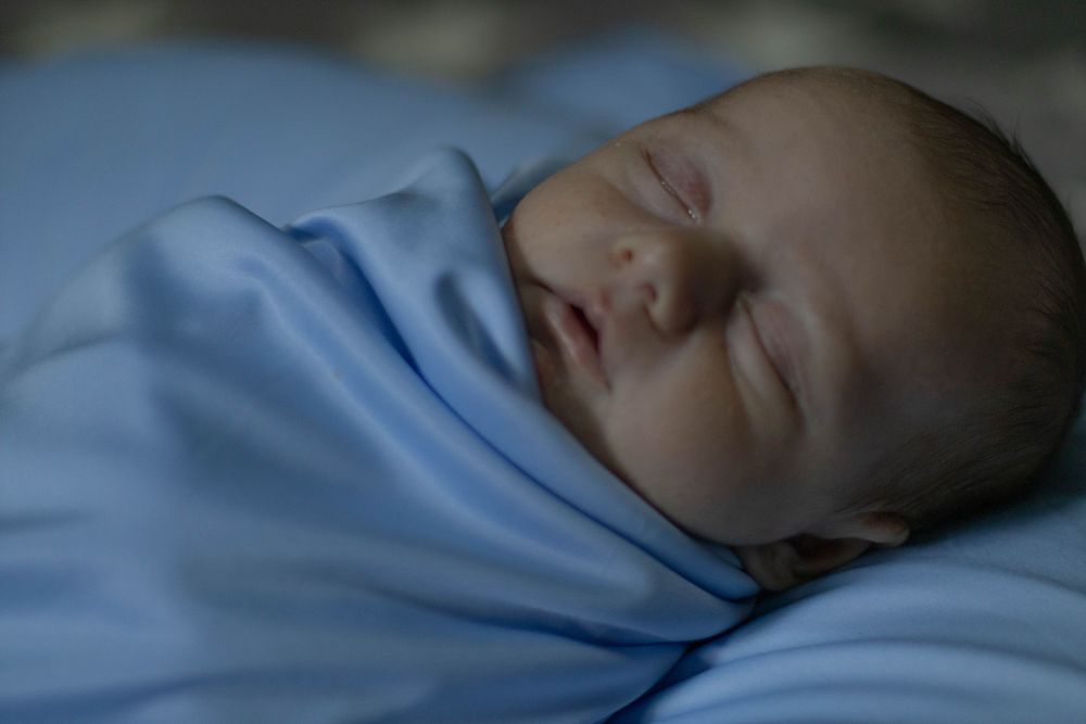 Peaceful newborn baby swaddled in a soft blue blanket sleeping soundly in a serene, dimly lit setting.