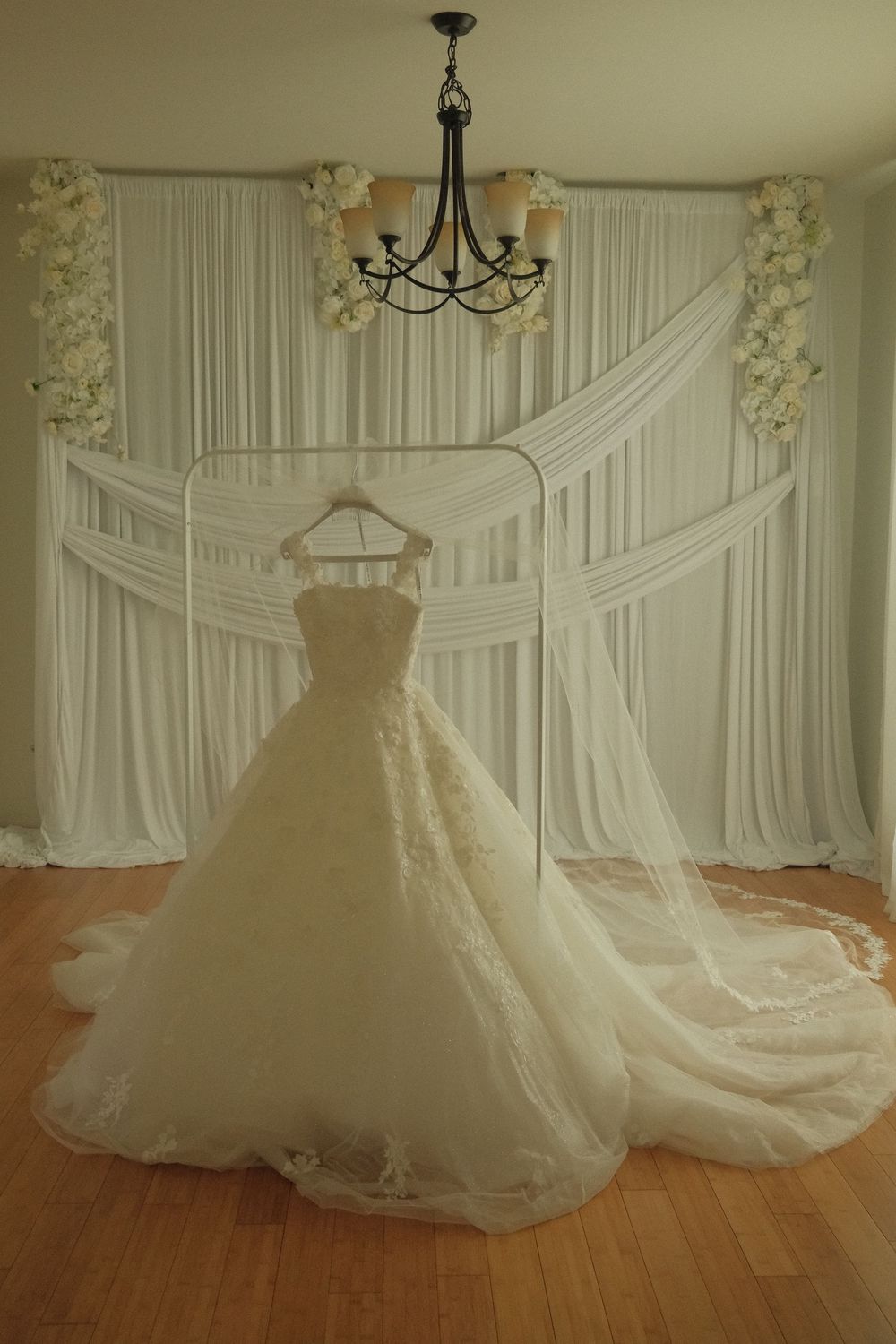 Elegant ivory A-line wedding gown with lace trim and cathedral train displayed on hanger against white draped backdrop.