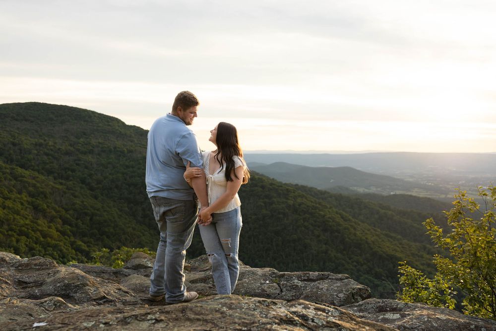 Couple standing on rocky mountain overlook enjoying scenic green valley views at sunset.