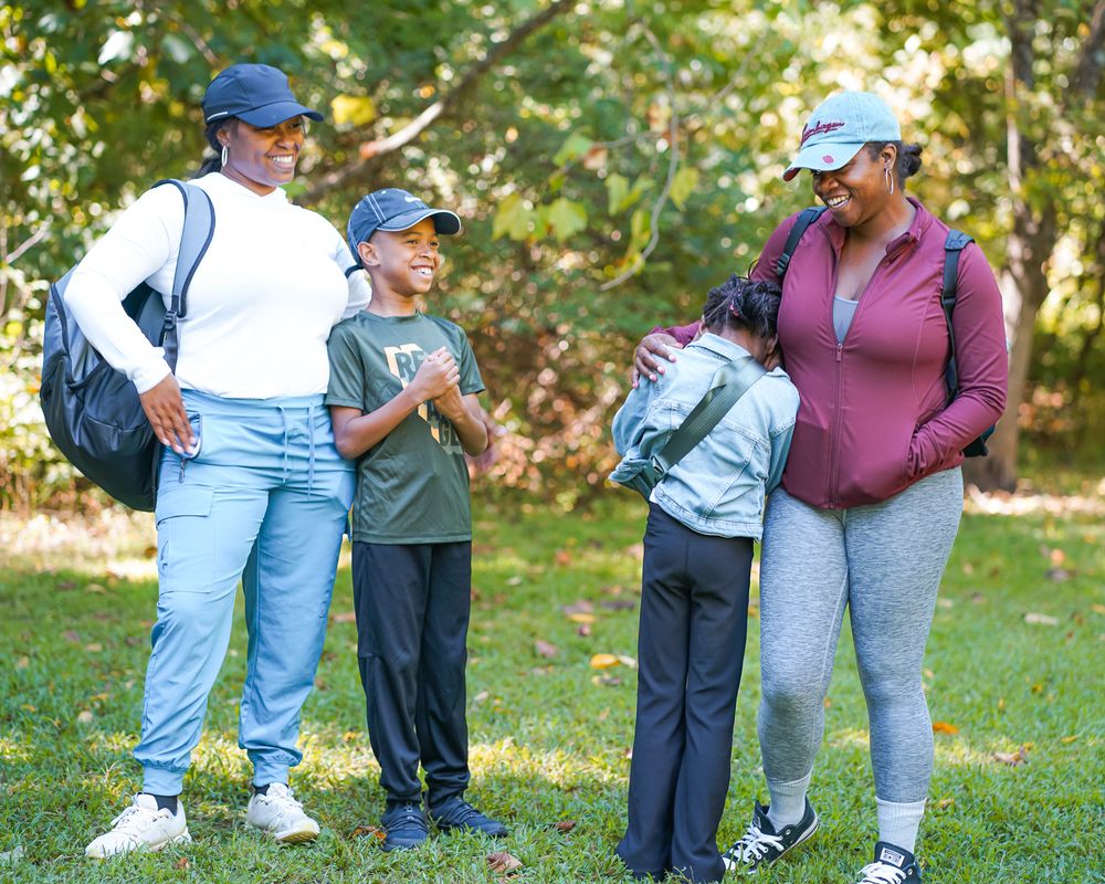 Two Black women and two boys laugh together outdoors on a sunny day in a green park.