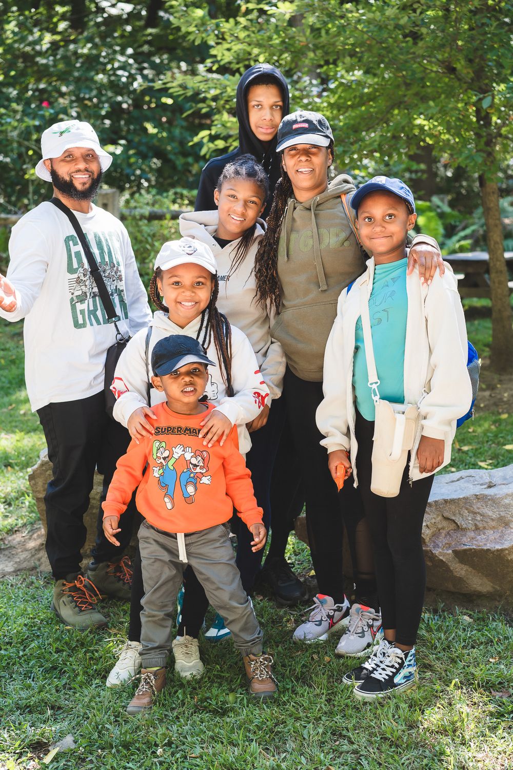 Black family with children poses together outdoors near rocks and trees on a sunny day.