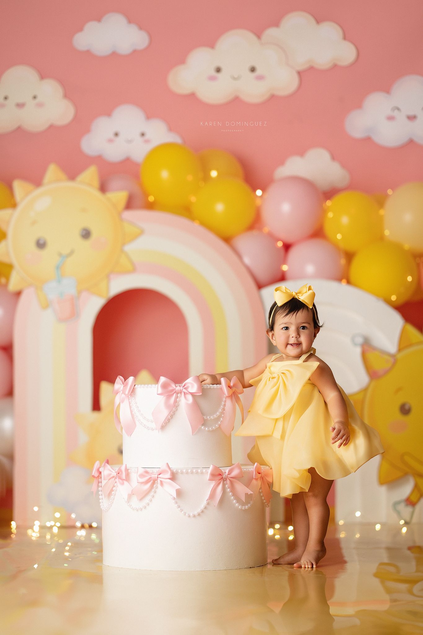 Toddler girl in fairy costume with wings poses in enchanted mushroom garden setting with butterflies and flowers.