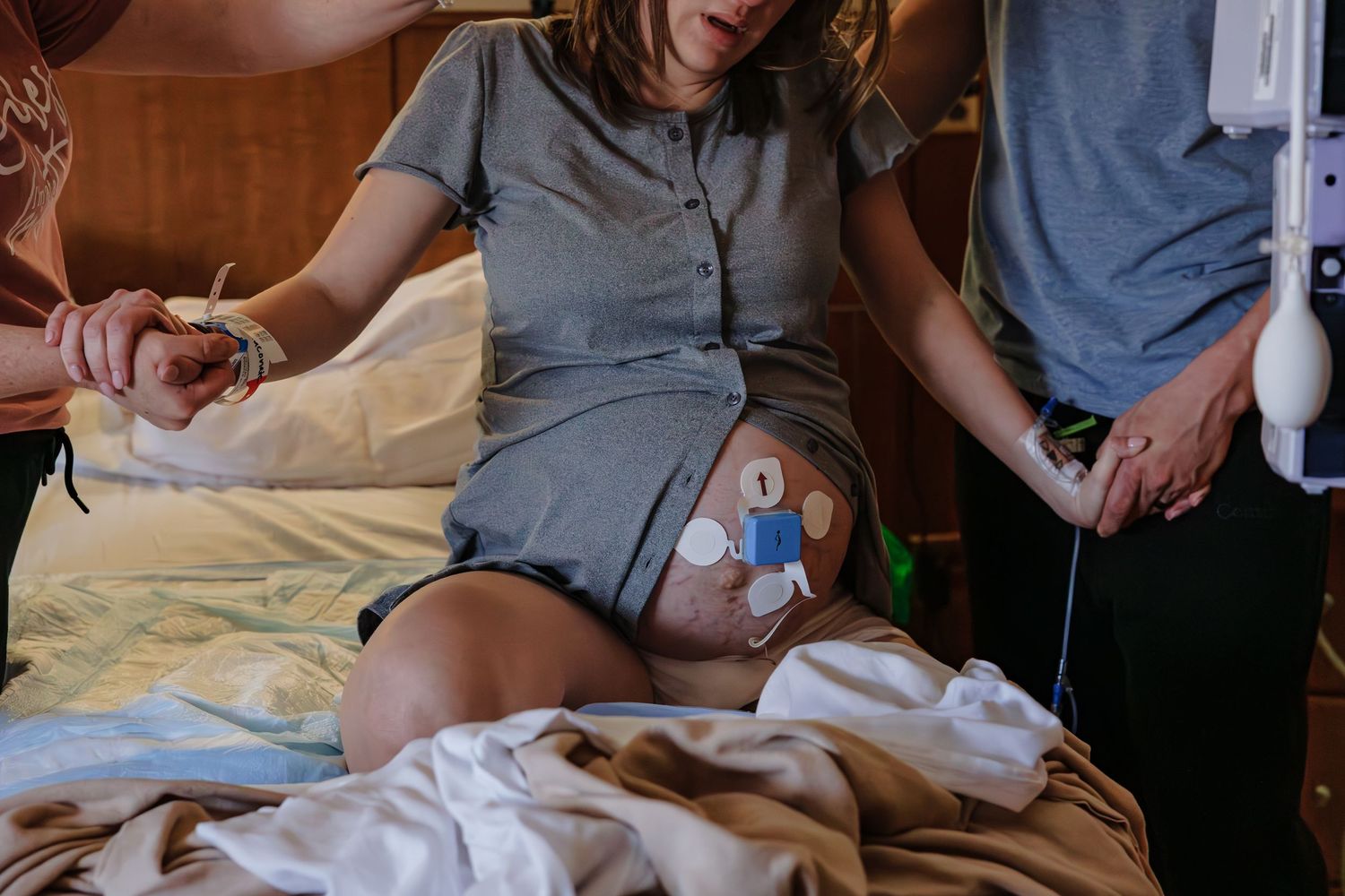 Pregnant woman sitting on hospital bed with fetal monitor attached, supported by medical staff during labor.