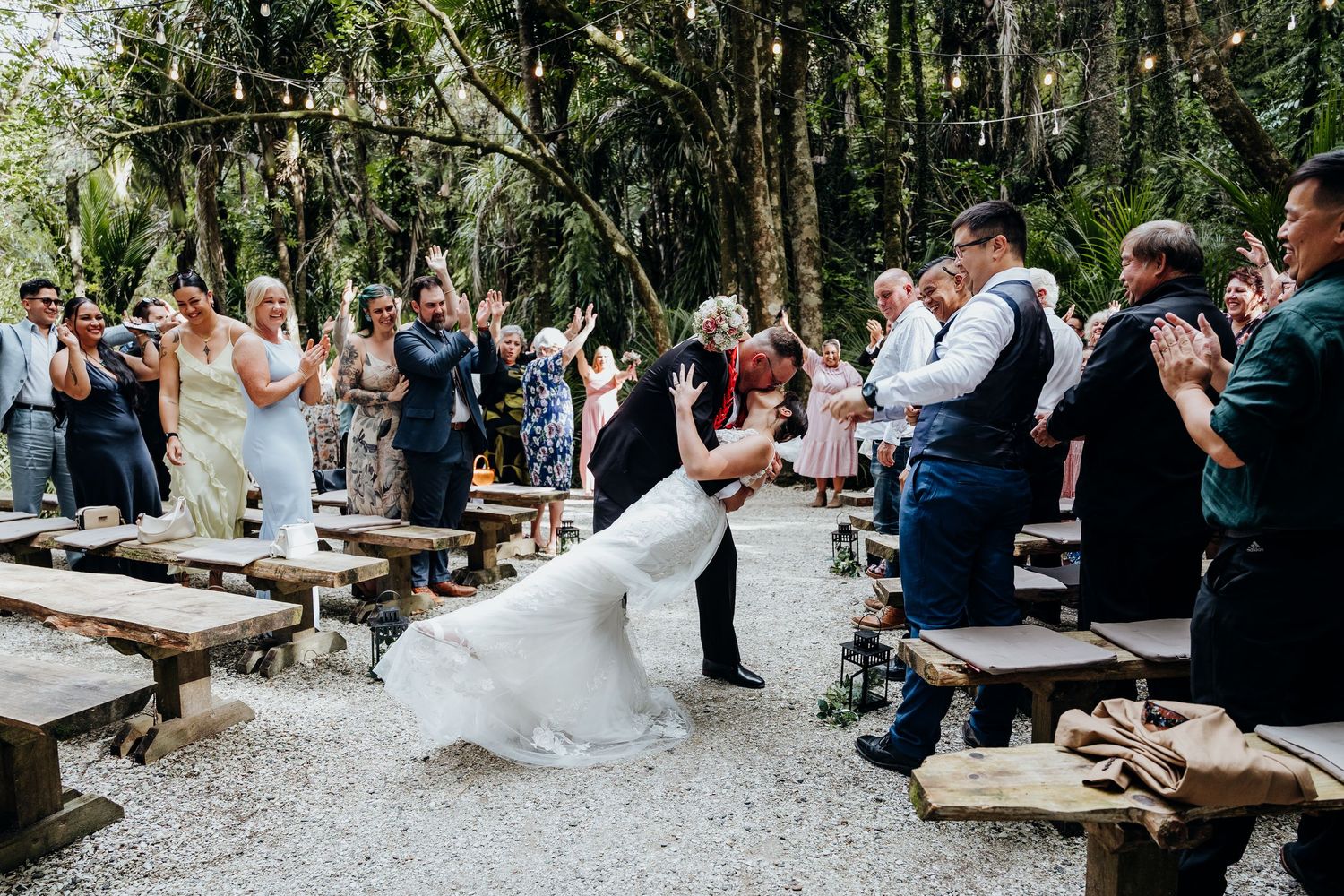 Newlyweds perform their first dance surrounded by guests in a warmly lit reception venue during their wedding celebration.
