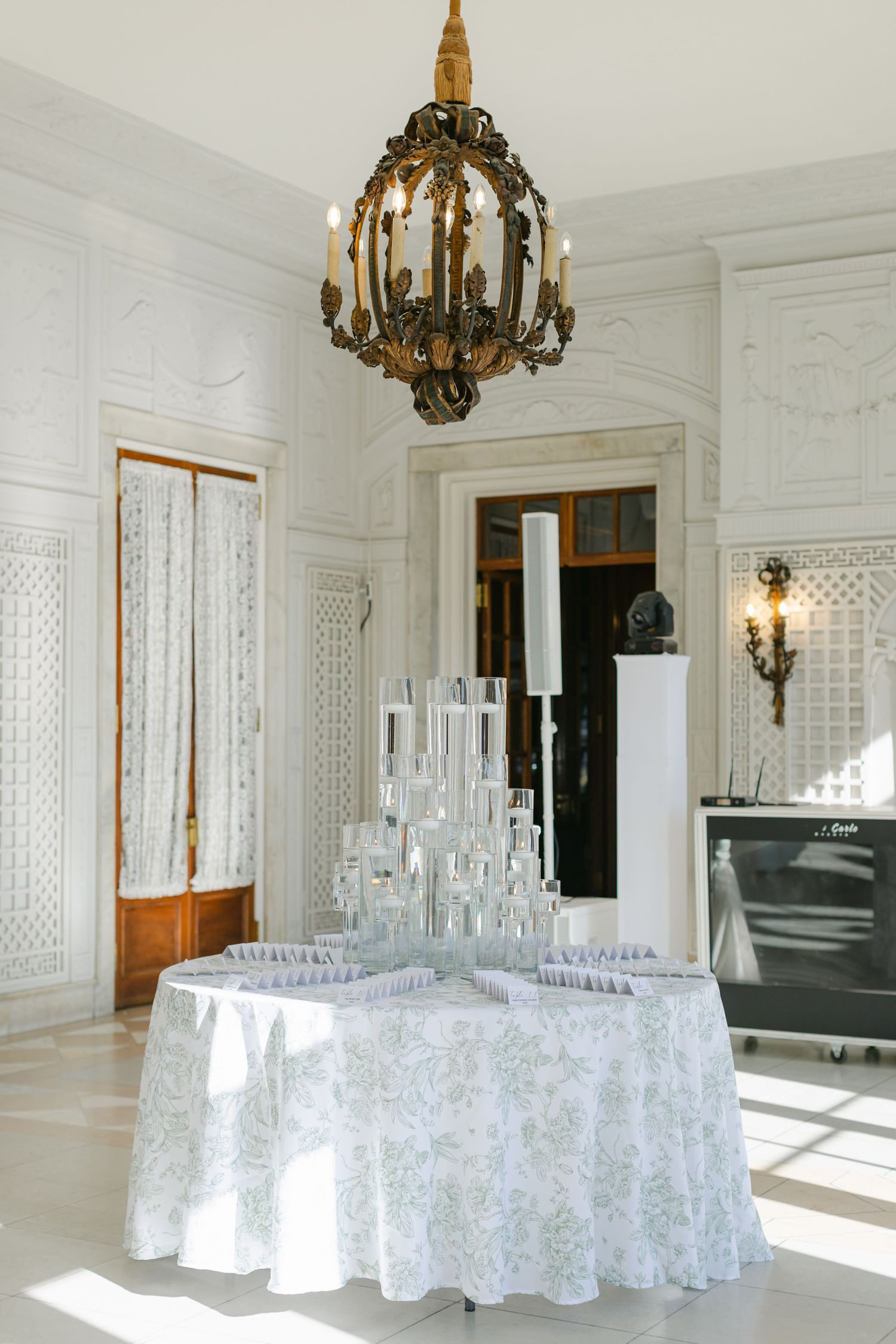 Armour House Wedding - Elegant white room with ornate chandelier and champagne glass tower on floral tablecloth for a wedding reception.