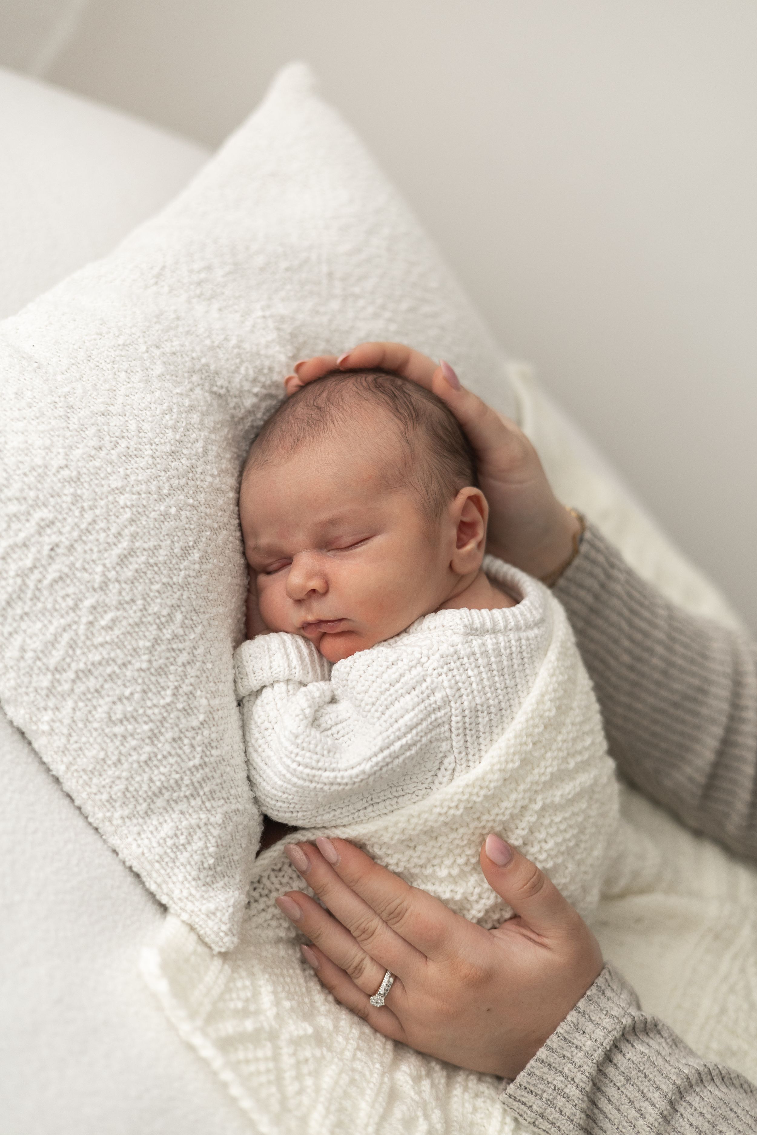 Newborn baby sleeping peacefully while being cradled gently by mother's hands during Newborn baby photographer Nottingham studio