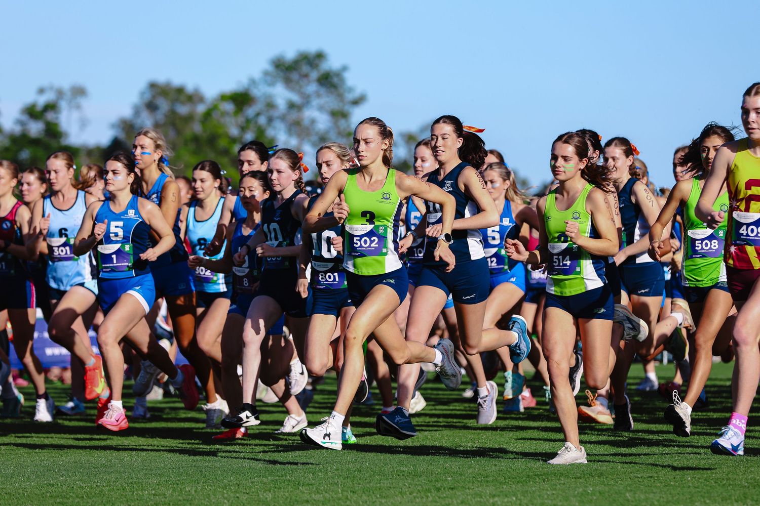 Two smiling athletes in blue jerseys numbered 5 and 6 with teal headbands pose proudly at an outdoor sports event.