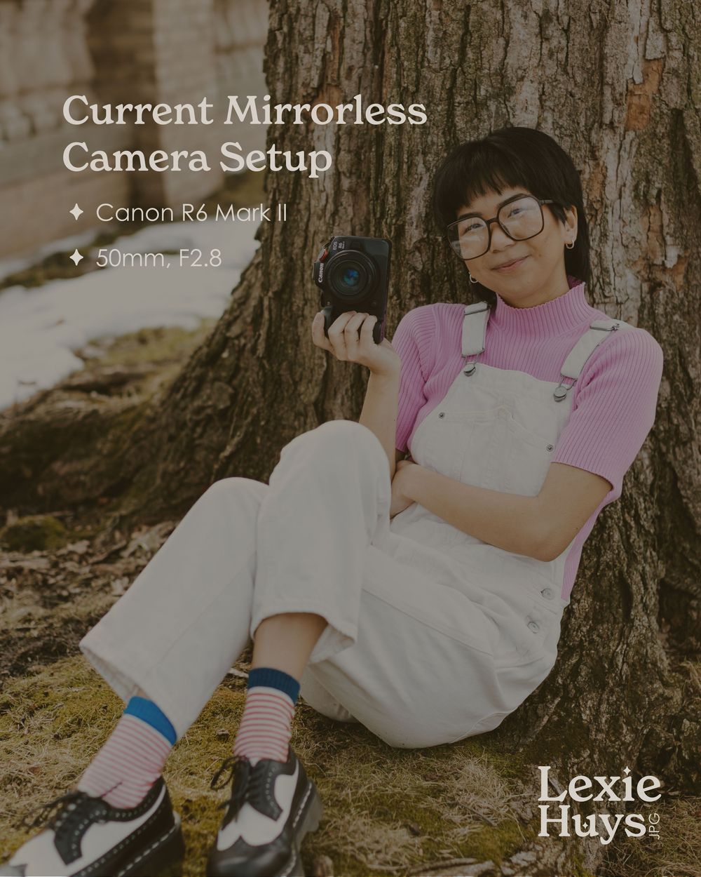 Lexie Huys sits against a tree holding a Canon R6 Mark II camera, wearing white overalls and pink turtleneck with colorful socks.