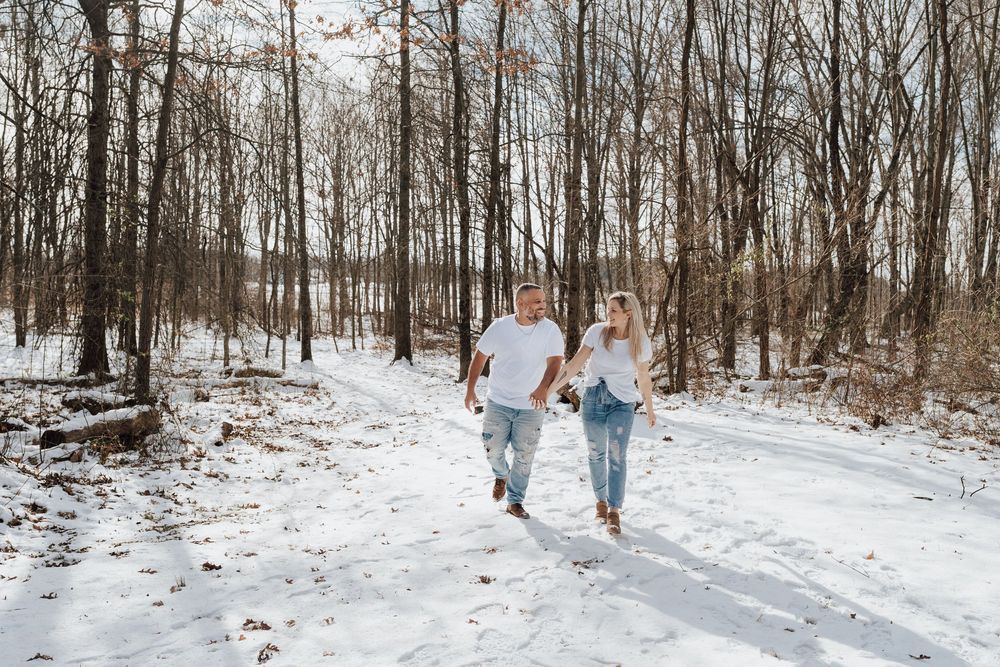 Couple holding hands running on a snowy forest path in winter, surrounded by bare trees.