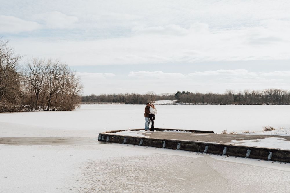 Couple embracing on the frozen Memorial Lake  dock in winter, taking engagement photos in Central PA