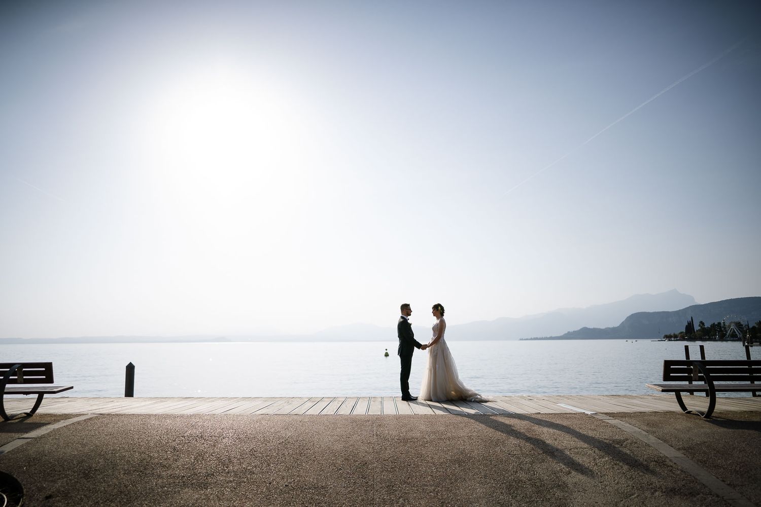 A romantic silhouette of newlyweds standing on a dock overlooking a misty lake and mountains.
