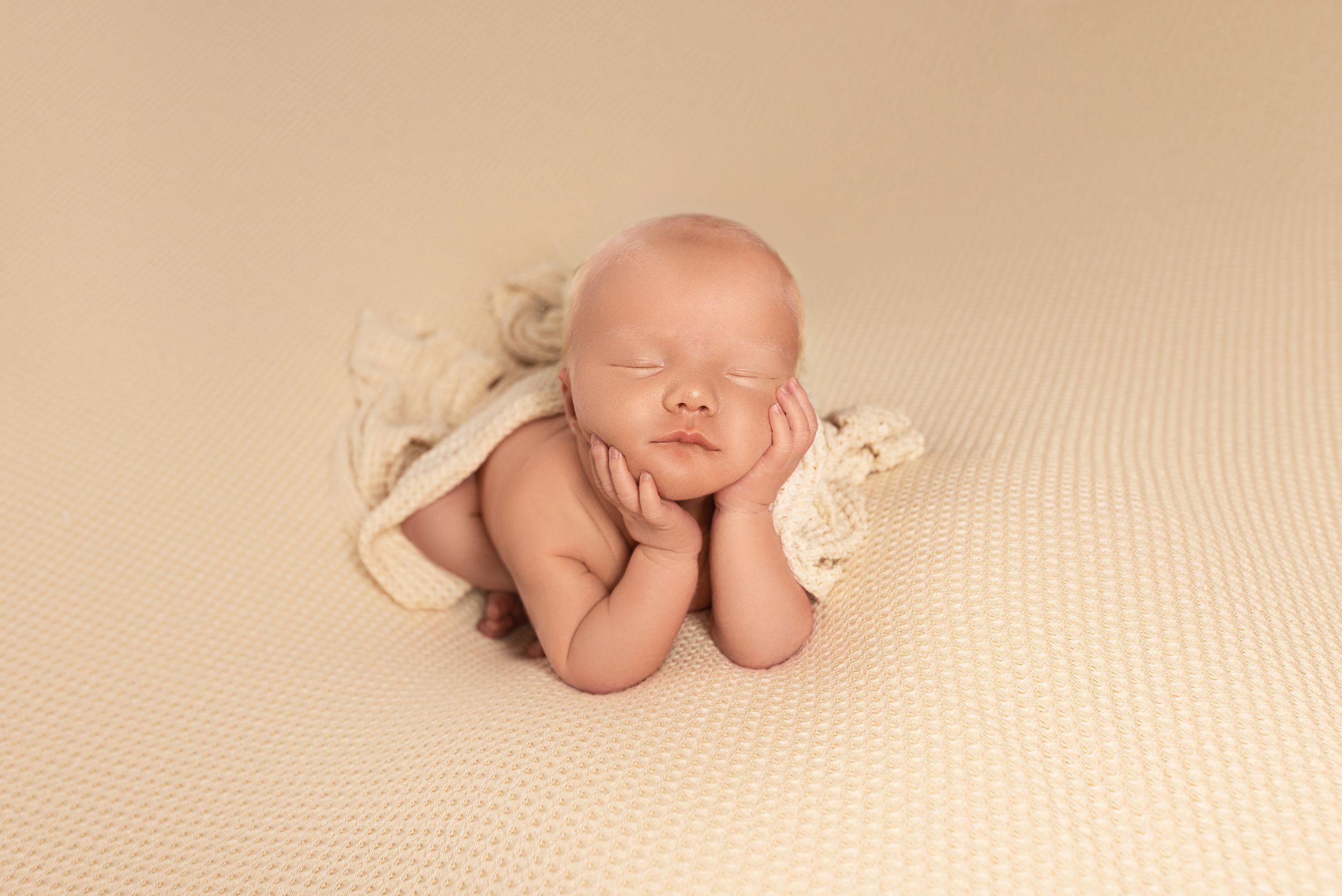 Peaceful sleeping newborn in cream wrap posed with hands under chin.