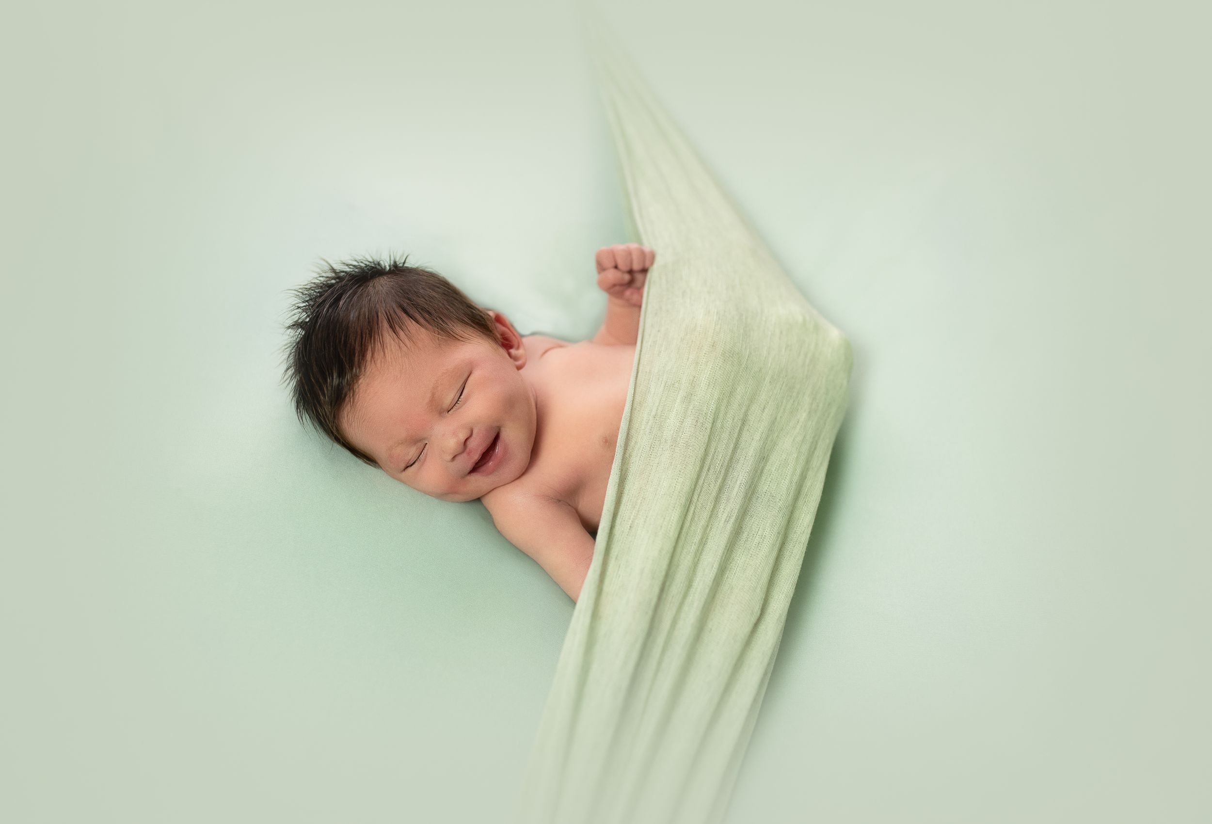 Artistic newborn portrait with soft green draping in minimalist style.