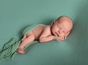 Newborn baby sleeping peacefully on mint green fabric in artistic pose.
