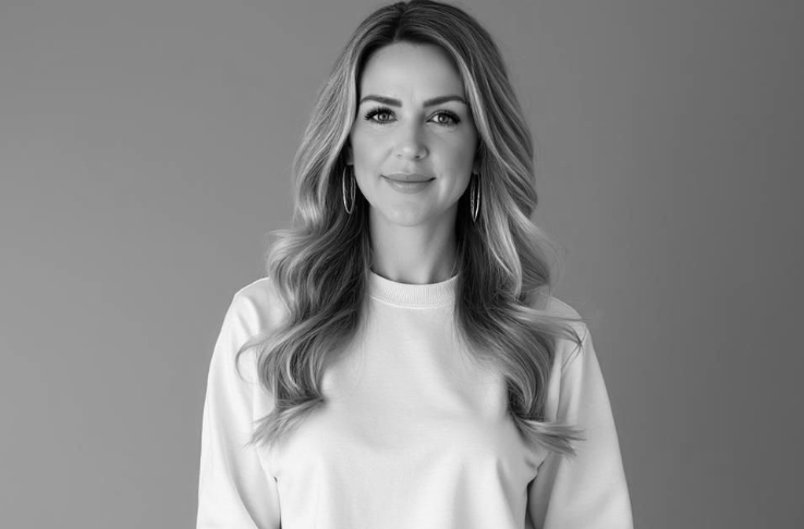 Black and white close-up portrait of a smiling woman with long wavy hair in a white sweatshirt.