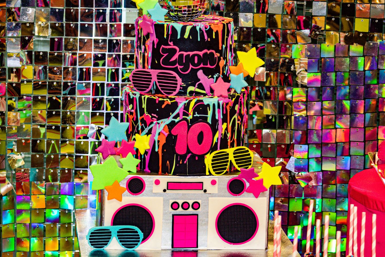 Neon 80s themed 10th birthday cake for Zyon with boombox decoration, colorful stars, and sunglasses on glitter backdrop.
