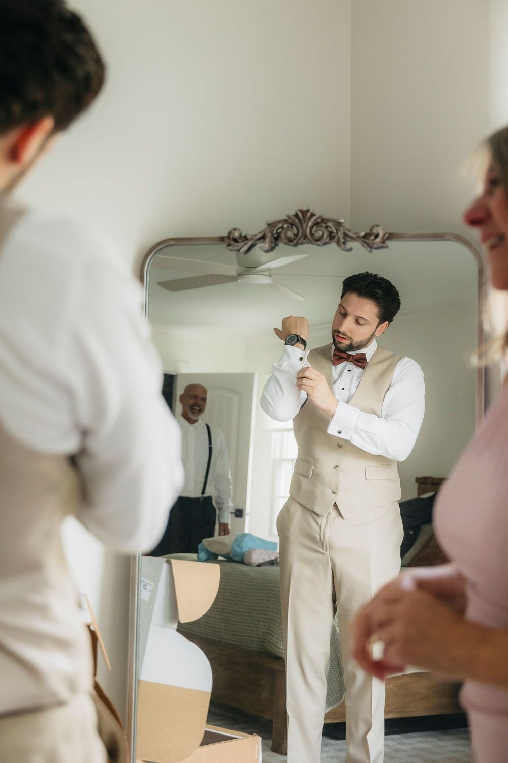 Groom in white shirt and beige vest adjusting cufflinks in ornate mirror while getting ready for wedding in Chicago