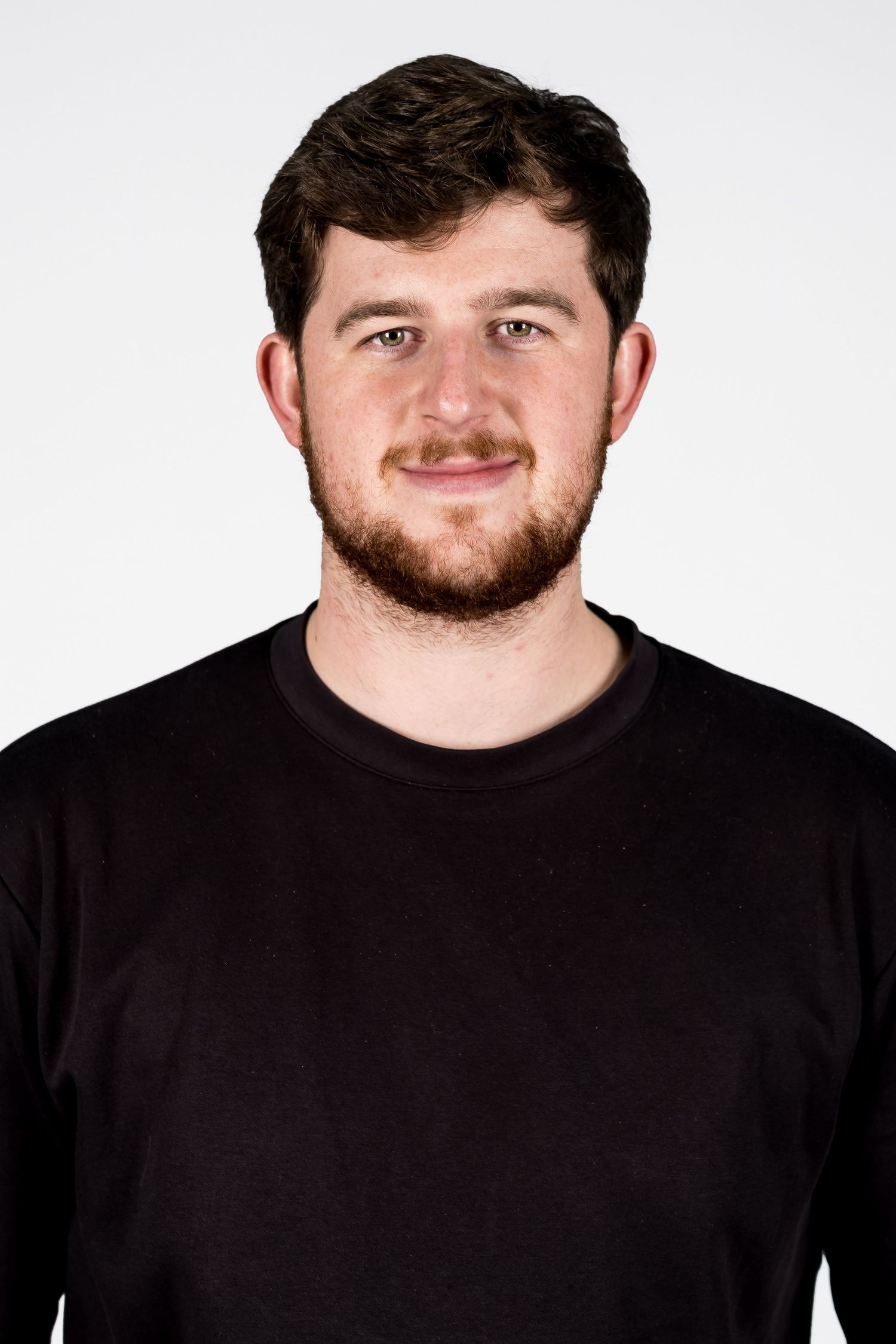 Young man with brown beard wearing a black long-sleeve shirt posing for a headshot photo against white background.