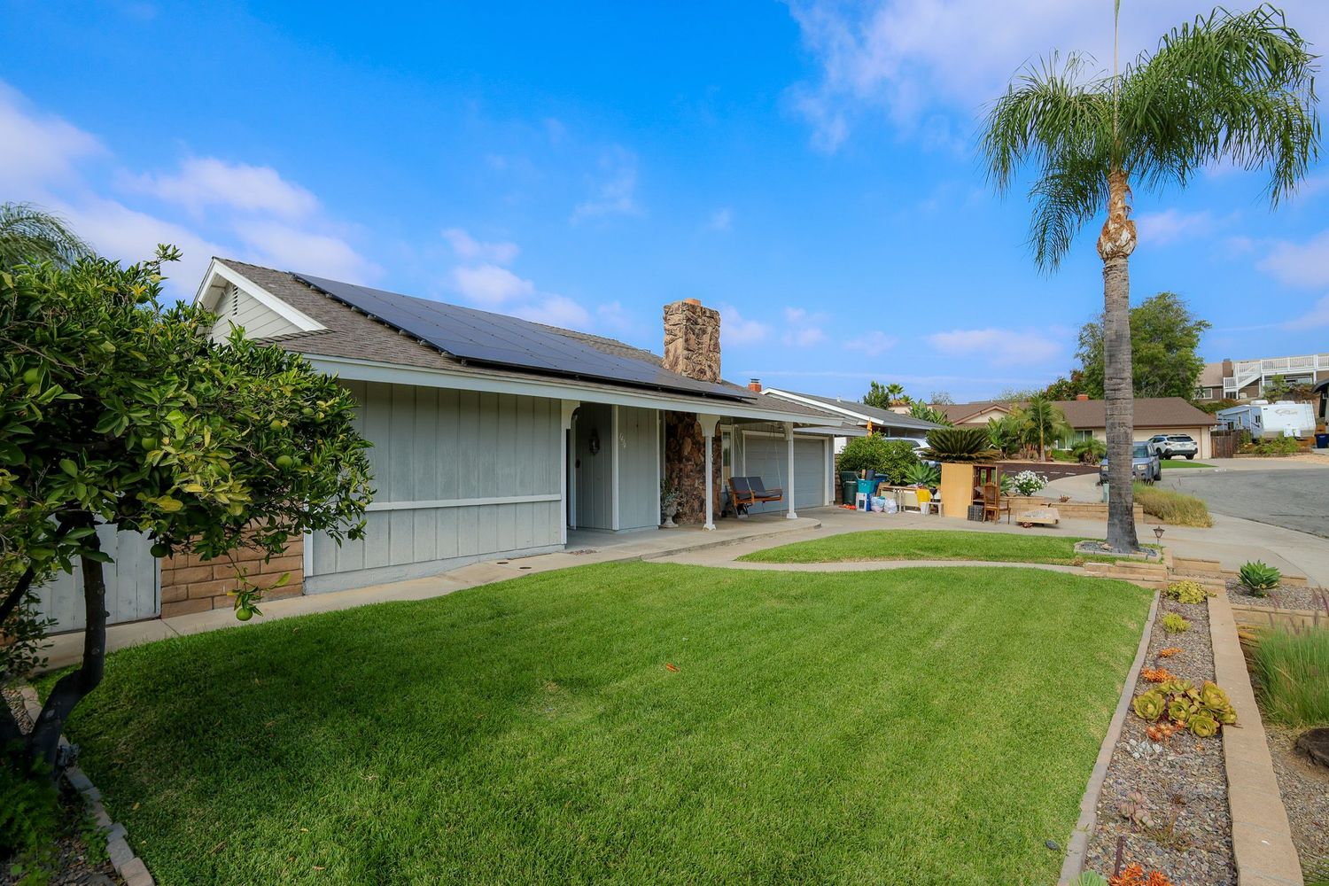 San Diego real estate photography of a suburban home with a green front lawn, solar panels, and a palm tree.