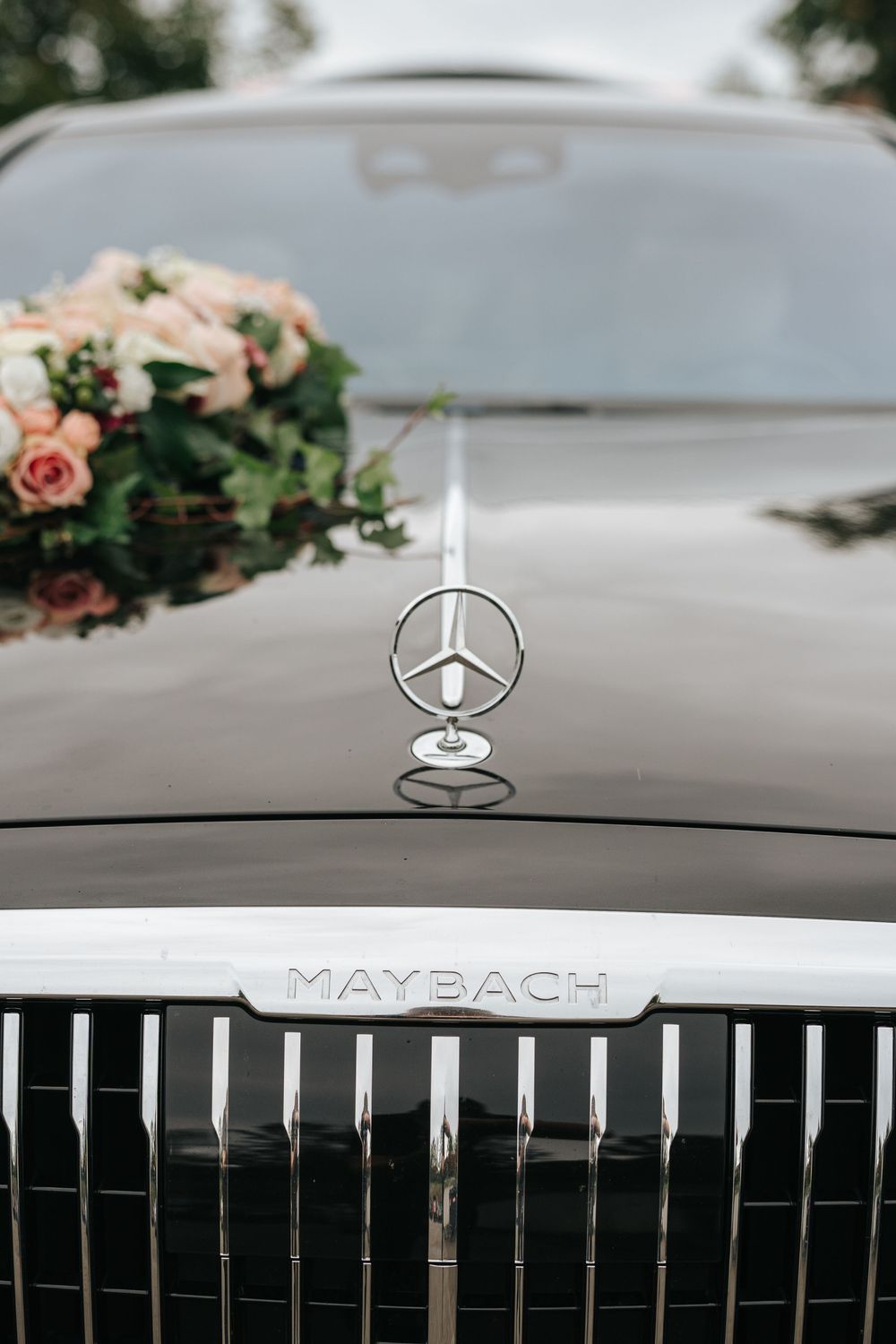 Mercedes-Maybach luxury car hood ornament with three-pointed star logo, adorned with a bridal flower bouquet on the hood.