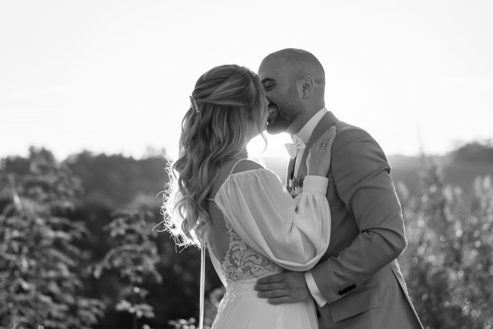 Black and white photo of a couple sharing a first kiss at their wedding ceremony outdoors.